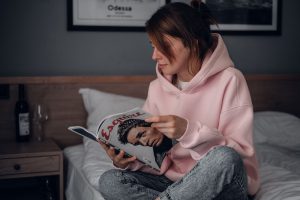 A woman in a pink hoodie reads a magazine in an Odesa bedroom.