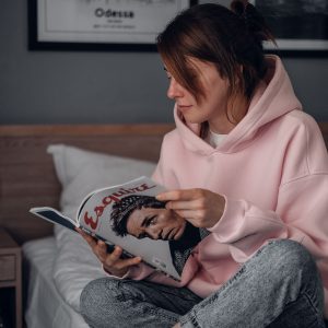A woman in a pink hoodie reads a magazine in an Odesa bedroom.